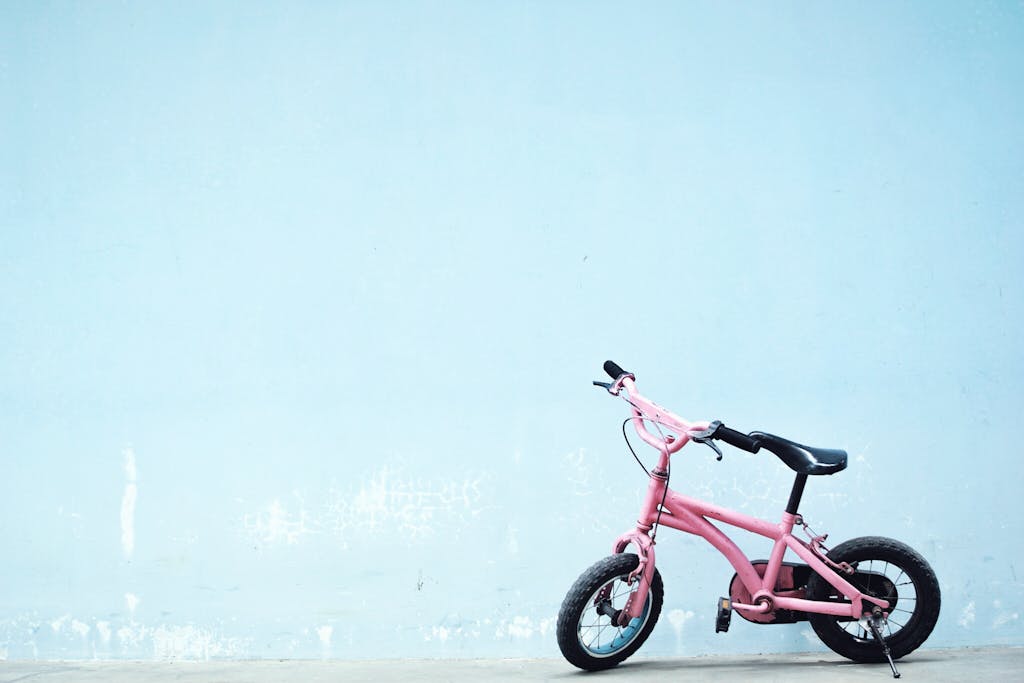 A pink child's bicycle leans against a simple blue wall, offering a whimsical urban scene.